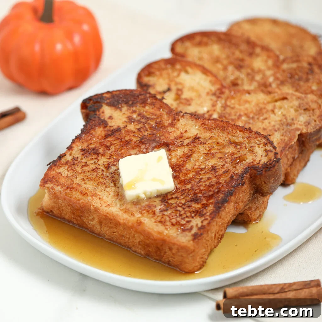 Three slices of French toast with syrup and a pat of butter on top are served on a white plate, with a small pumpkin and cinnamon sticks nearby.