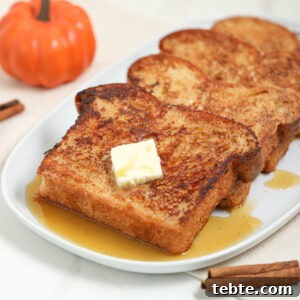 Three slices of French toast with syrup and a pat of butter on top are served on a white plate, with a small pumpkin and cinnamon sticks nearby.