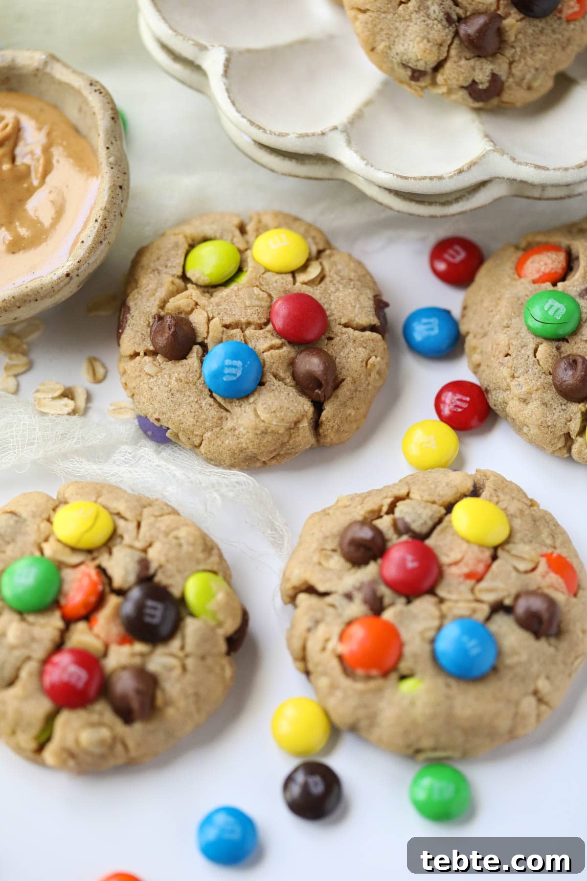 Soft Chewy Monster Cookies with Chocolate, Oats & Peanut Butter 3 monster cookies lying on a white tables with m&m's scattered around.