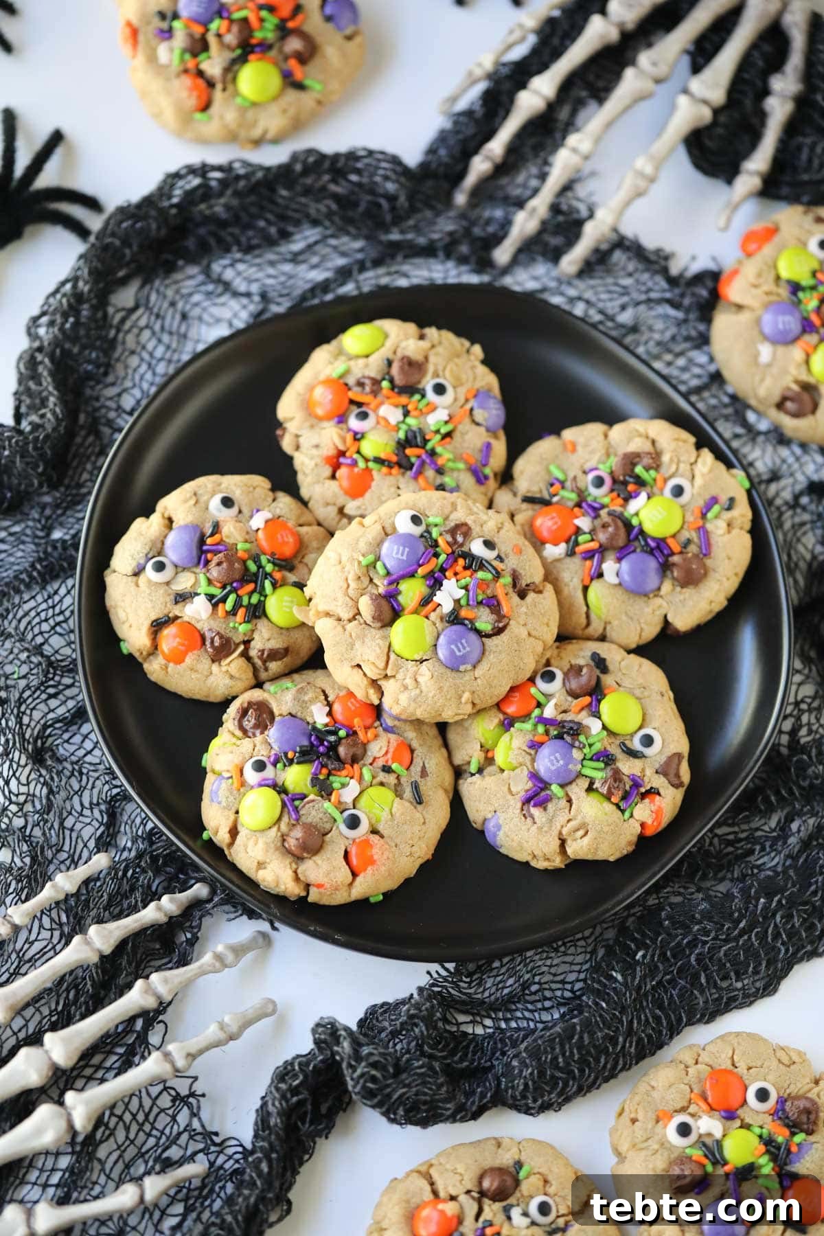 Soft Chewy Monster Cookies with Chocolate, Oats & Peanut Butter 8 monster cookies on a black plate with skeleton hands around the plate.