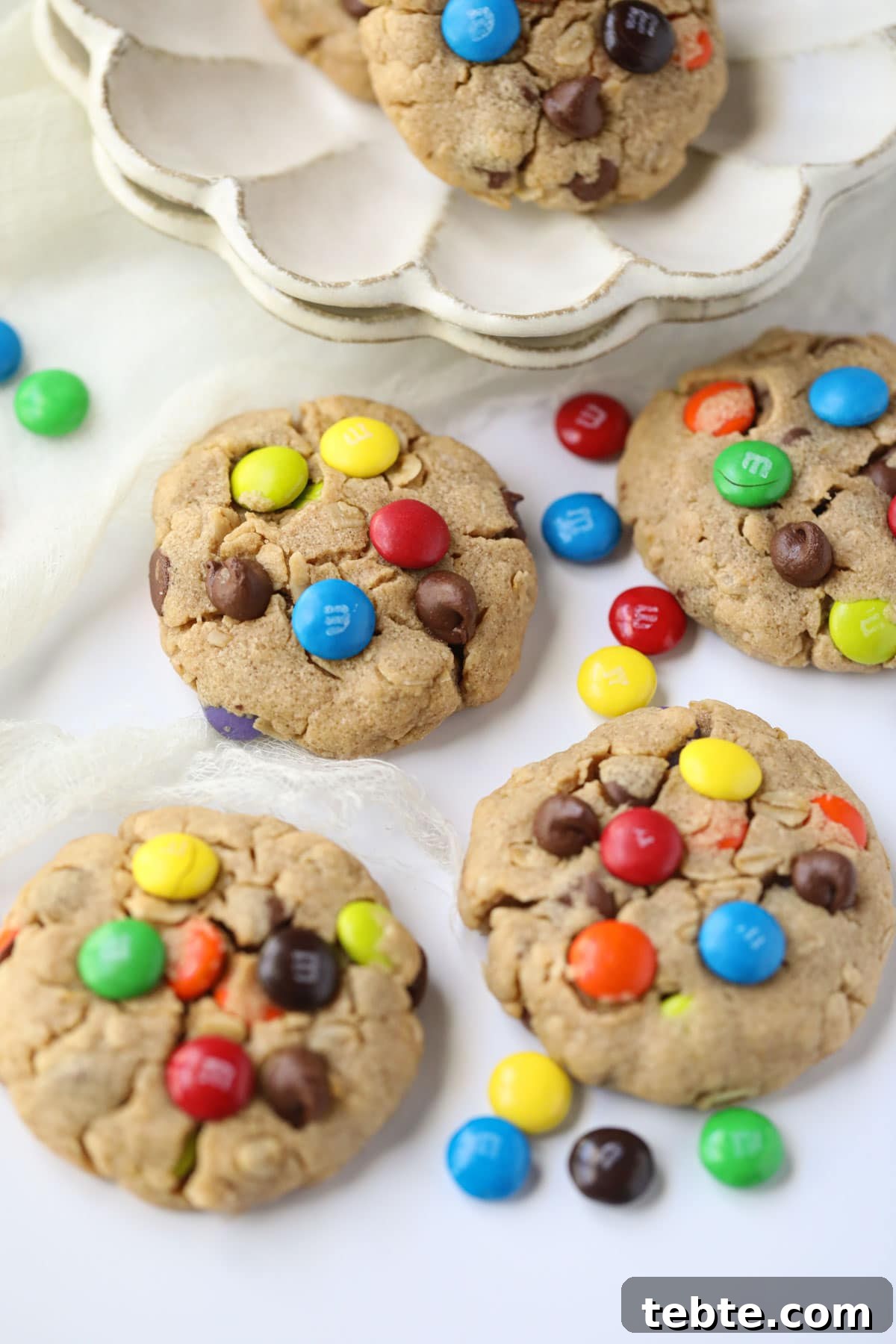 Soft Chewy Monster Cookies with Chocolate, Oats & Peanut Butter 9 monster cookies scattered on a white table.
