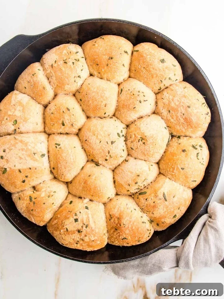Cast iron skillet filled with round herby dinner rolls.