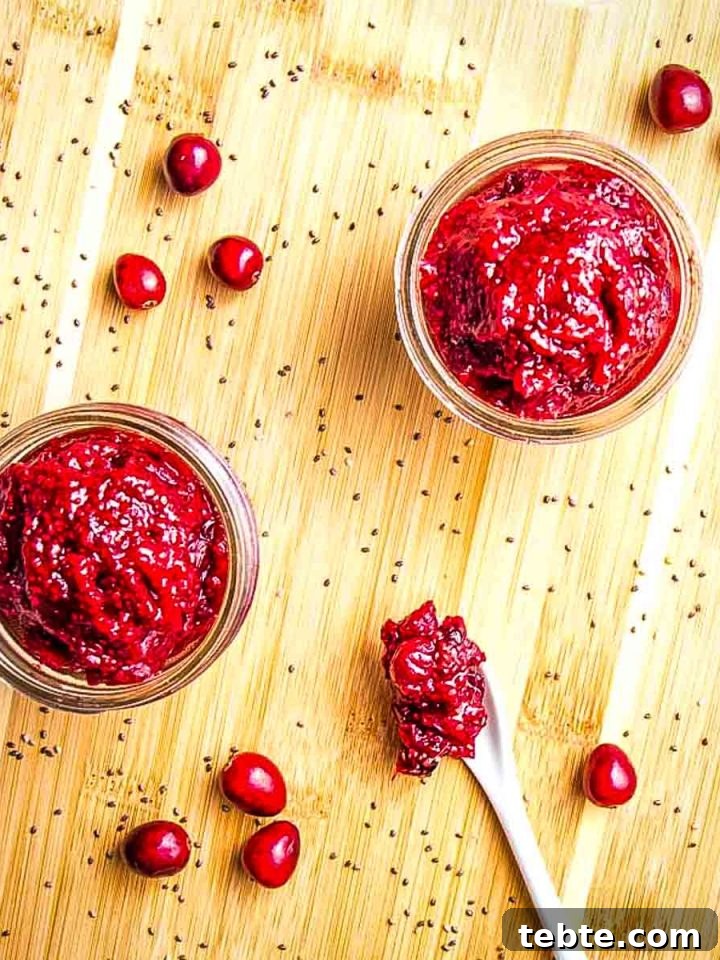 Cranberry jam in small jars with fresh cranberries, a spoonful of jam and a sprinkle of chia seeds on the cutting board.