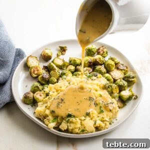 Creamy Vegan Mushroom Gravy Recipe 16 White pitcher pouring gravy over plate of chunky mashed potatoes and brussels sprouts