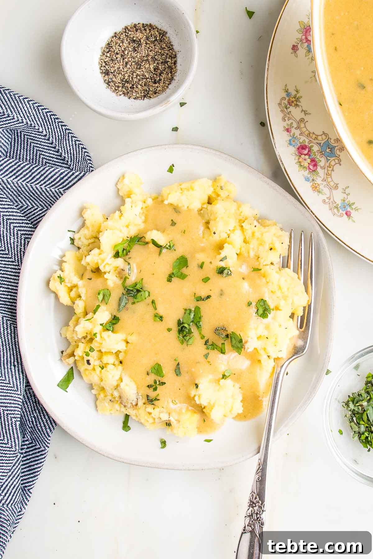 Creamy Vegan Mushroom Gravy Recipe 3 Plate full of mashed potatoes covered in vegan gravy and sprinkled with fresh herbs.