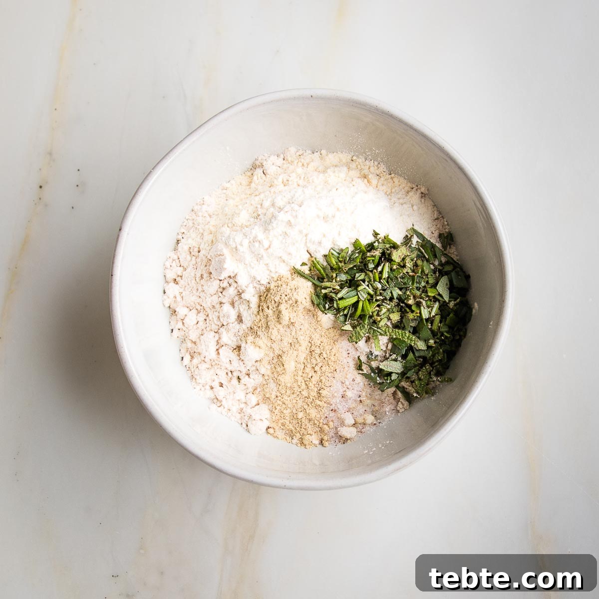 Creamy Vegan Mushroom Gravy Recipe 5 Small white bowl with flour, fresh herbs, arrowroot powder, salt, white pepper, garlic powder and onions powder.