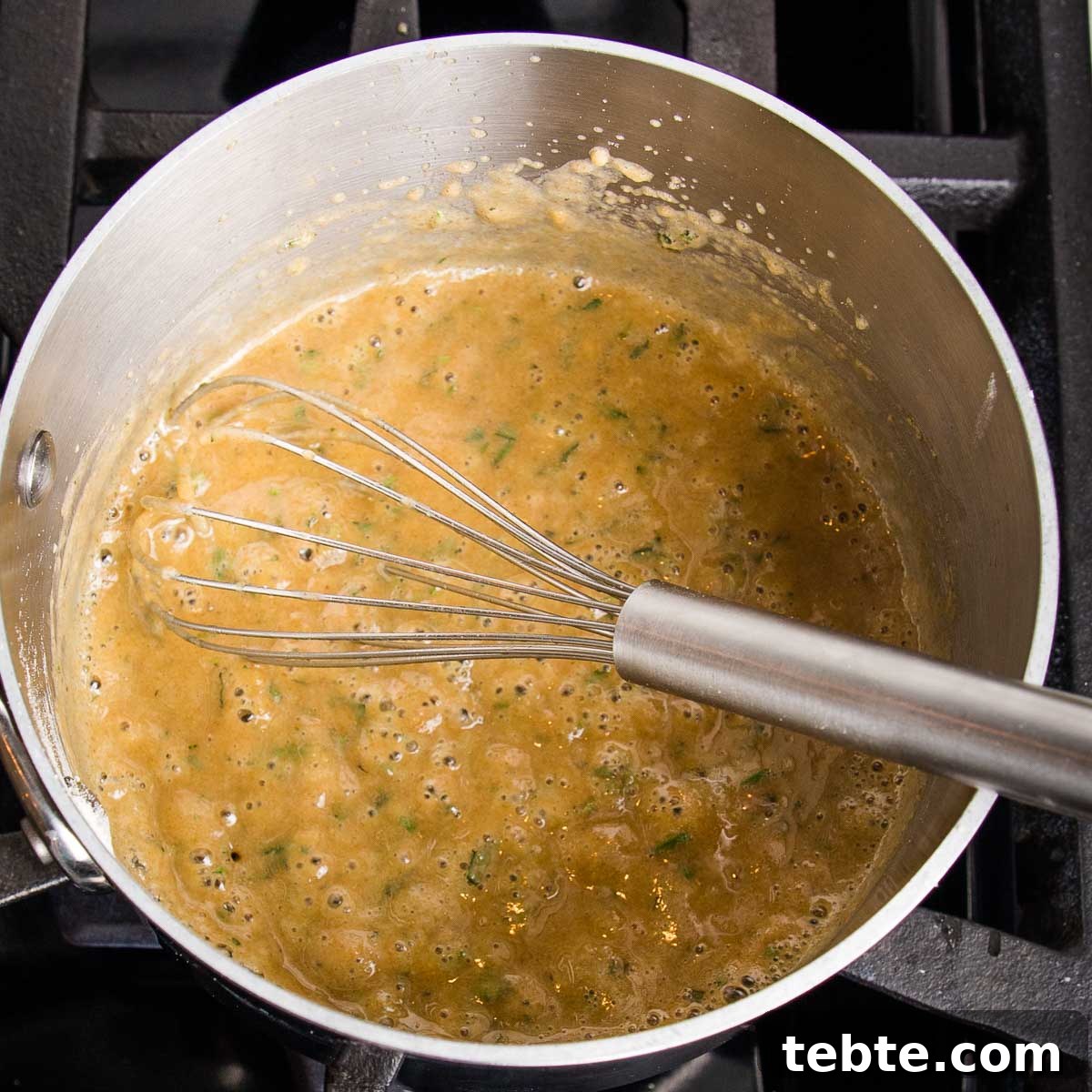 Creamy Vegan Mushroom Gravy Recipe 7 Small saucepan with a pasty mixture being whisked together. It's golden in color, speckled with flakes of fresh herbs.