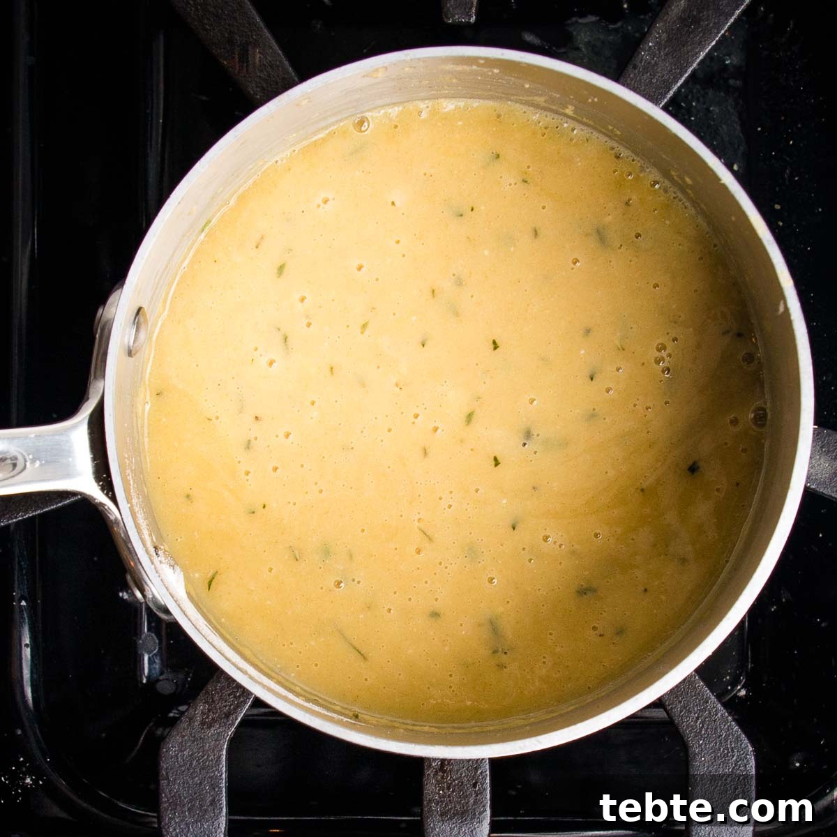Creamy Vegan Mushroom Gravy Recipe 9 Saucepan filled with golden gravy that's speckled with fresh herbs.