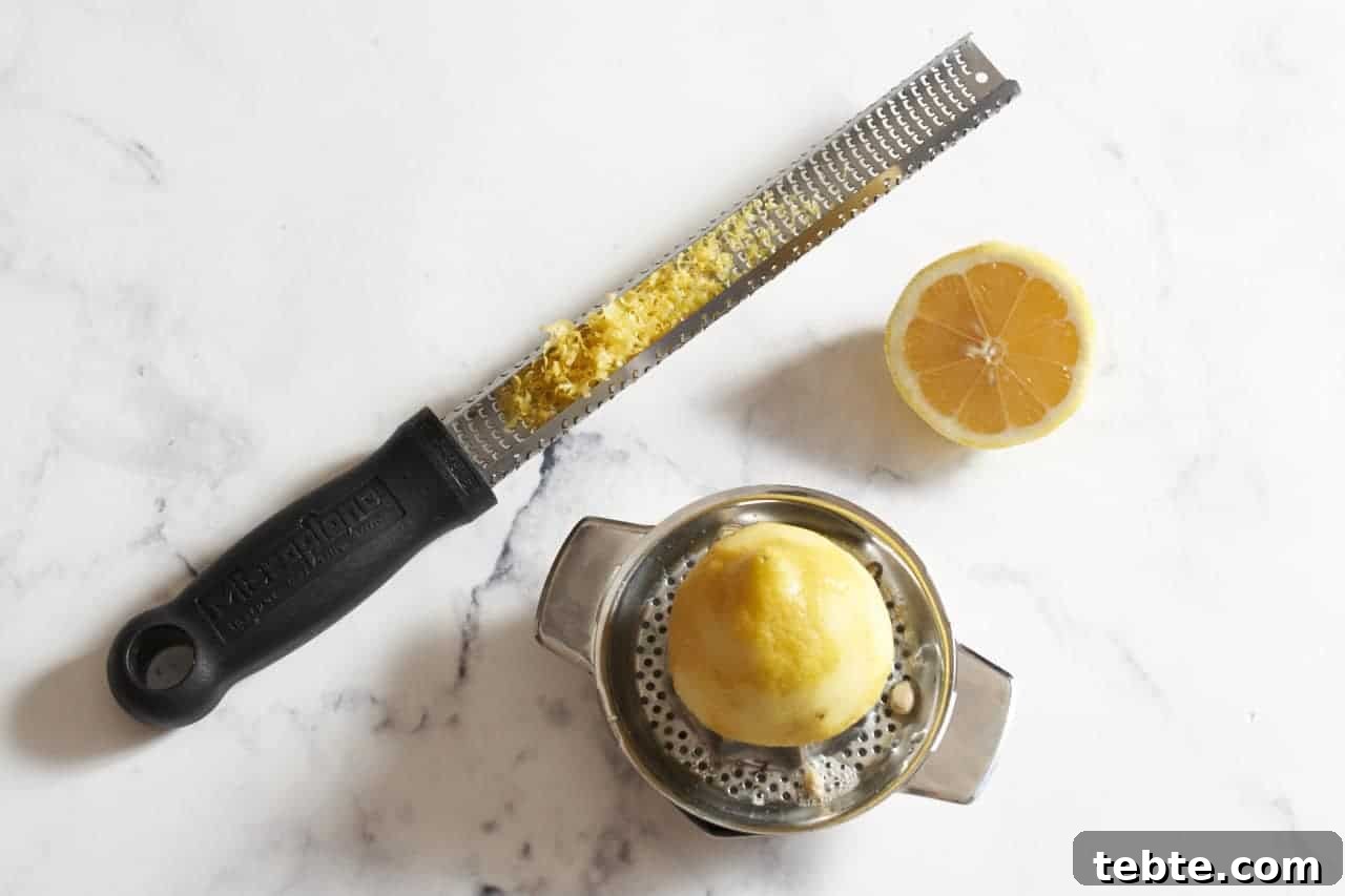 A microplane grater with lemon zest, and half a lemon on a small juicer.