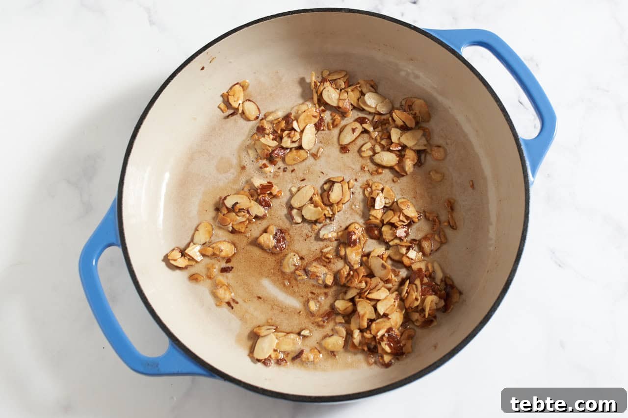 Sliced almonds and brown butter in a pan with blue handles.