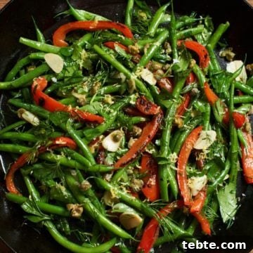 Fresh green bean salad with red peppers, capers and herbs in a skillet.