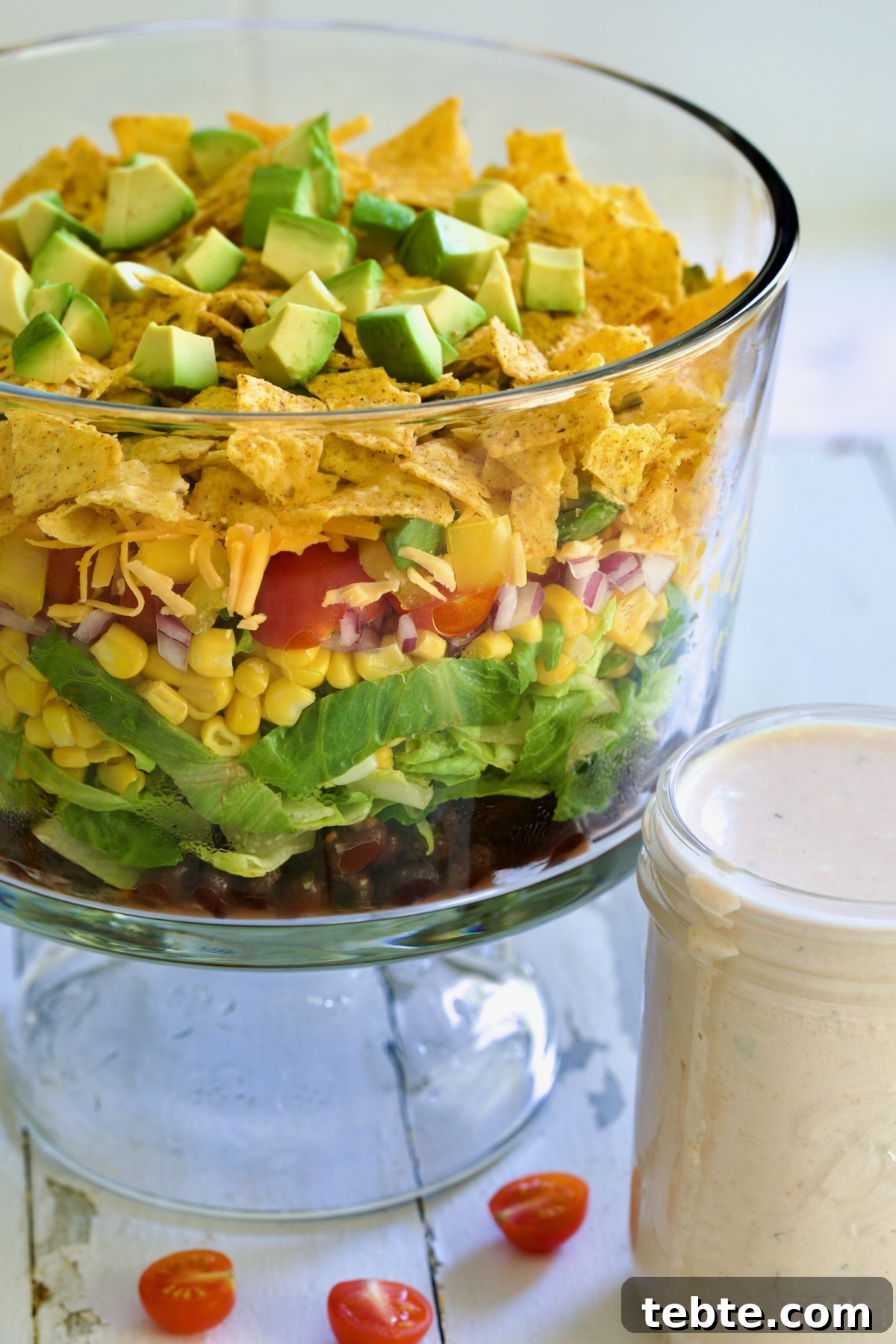 Layered Southwestern Salad with Corn, Black Beans, and Avocado 8 Southwestern Layered Salad in glass footed bowl with salad dressing in glass jar.