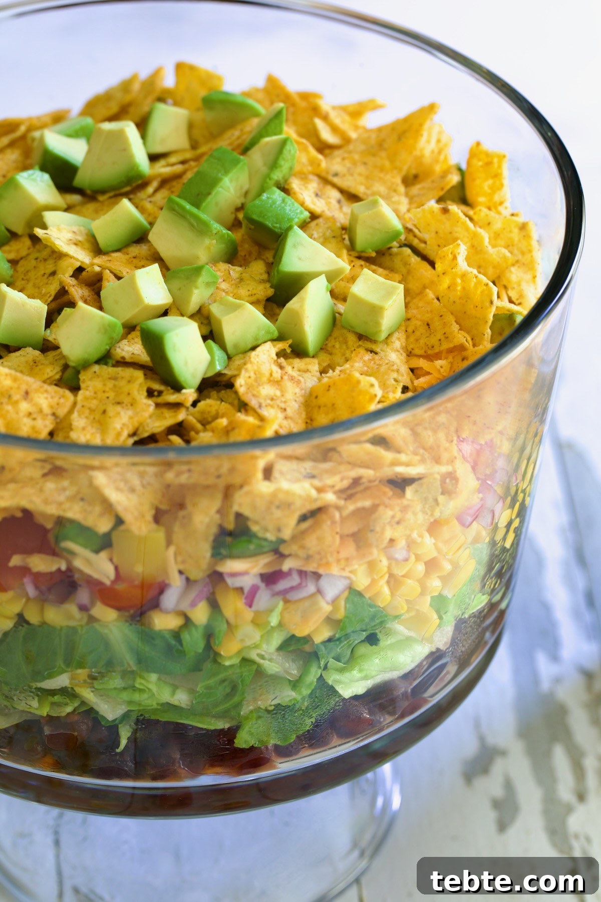 Layered Southwestern Salad with Corn, Black Beans, and Avocado 10 Southwestern Layered Salad in glass footed bowl.