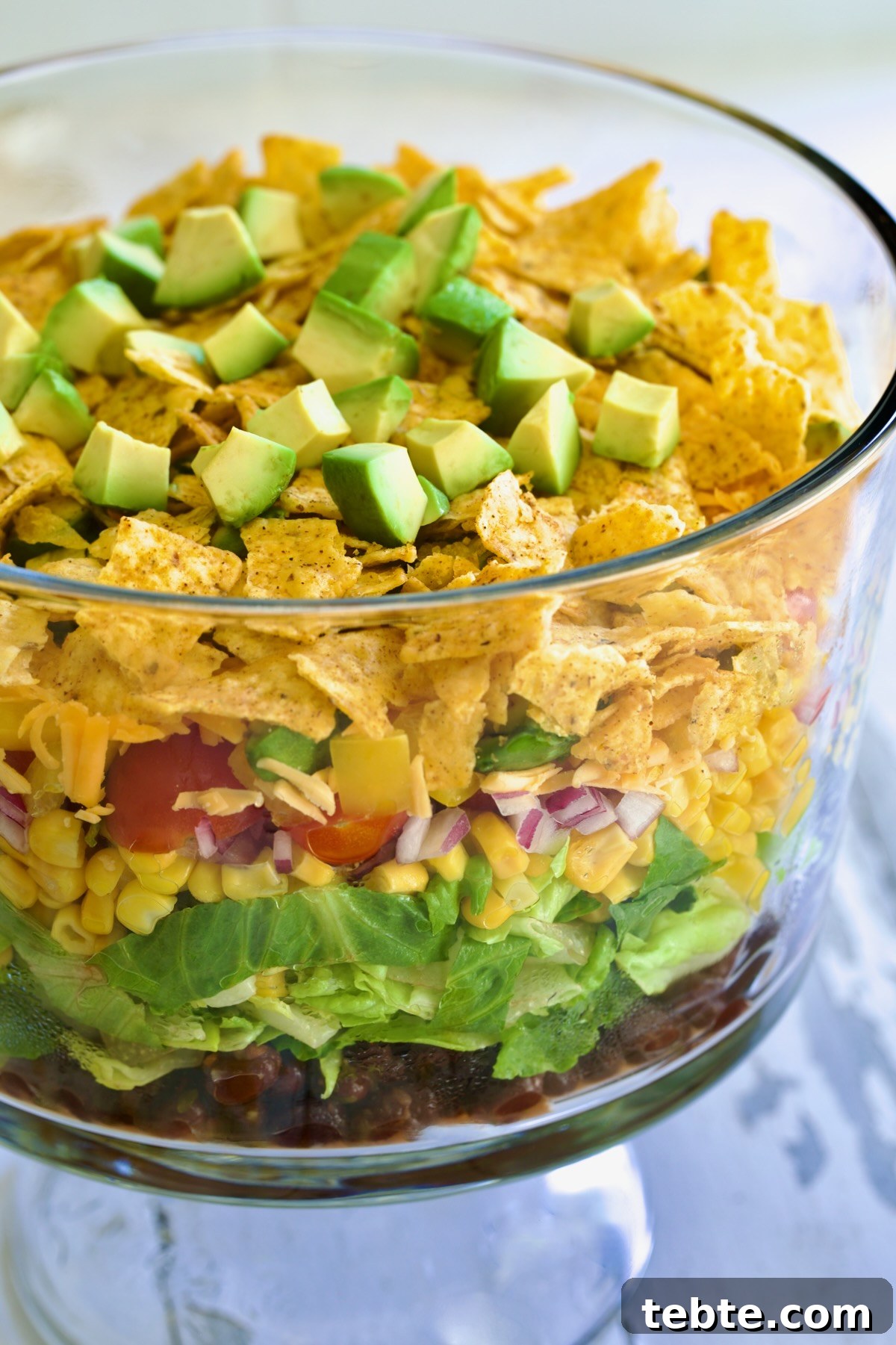 Layered Southwestern Salad with Corn, Black Beans, and Avocado 3 Southwestern Layered Salad in glass footed bowl.