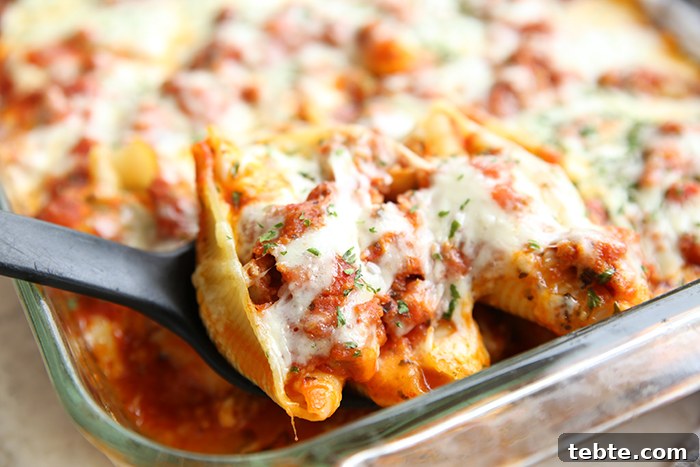 Fancy-Looking Christmas Eve Dinner Ideas for Busy Families 3 A glass 9x13 baking dish filled with stuffed shells with a black serving spoon scooping out some shells from the corner.