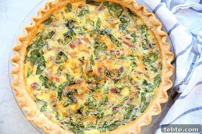 Fancy-Looking Christmas Eve Dinner Ideas for Busy Families 8 A 9-inch glass pie dish of Quiche with a white kitchen towel with blue stripes.