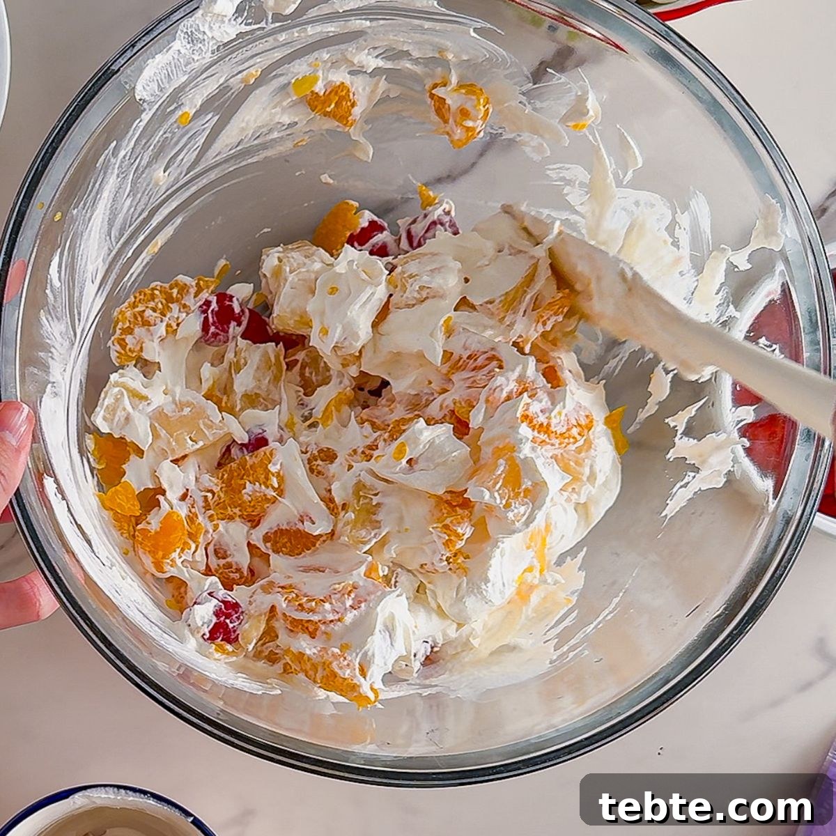 Classic Ambrosia Salad Recipe with Citrus and Coconut 6 Mixing the fruit into ambrosia salad.