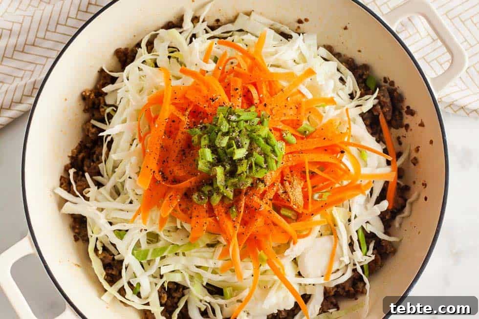 Keto Egg Roll in a Bowl: Low-Carb One-Pan Recipe 3 shredded carrots and shredded cabbage on top of cooked pork sausage in a bowl