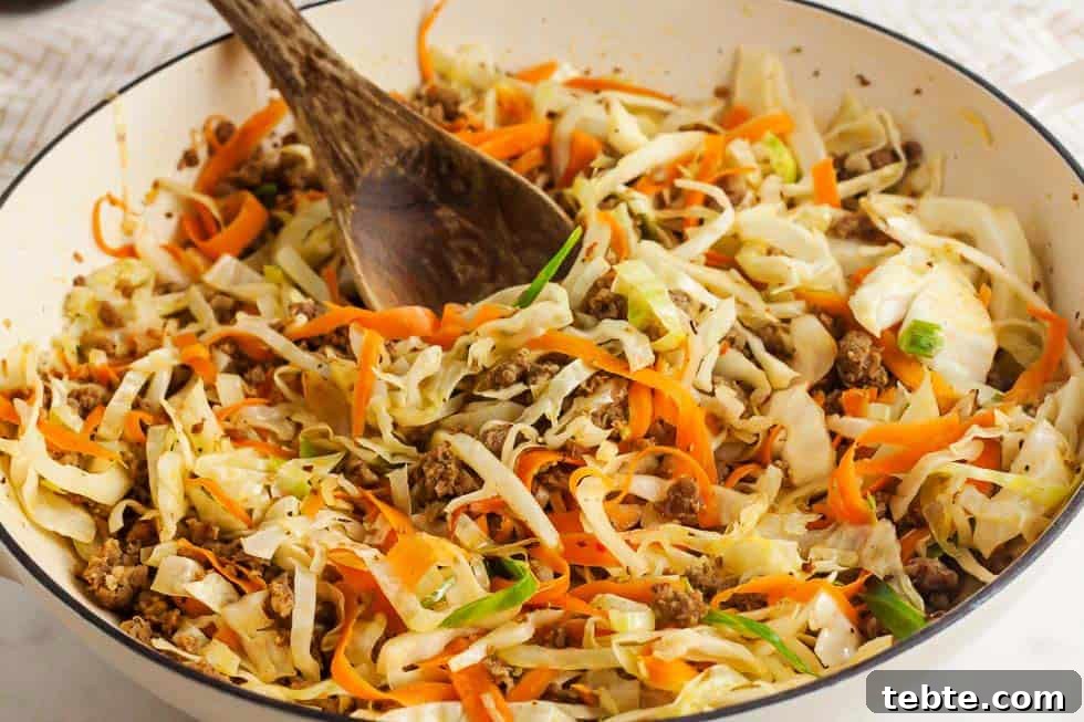 Keto Egg Roll in a Bowl: Low-Carb One-Pan Recipe 4 wooden spoon inside of a bowl containing cooked shredded cabbage with carrots and pork