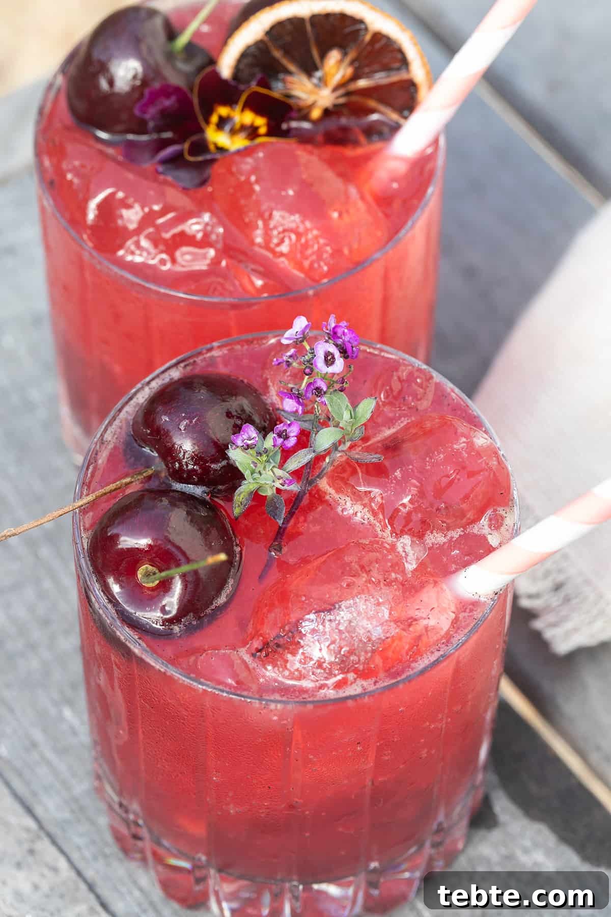 A cherry gin soda with cherries, edible flowers and a stripy straw.